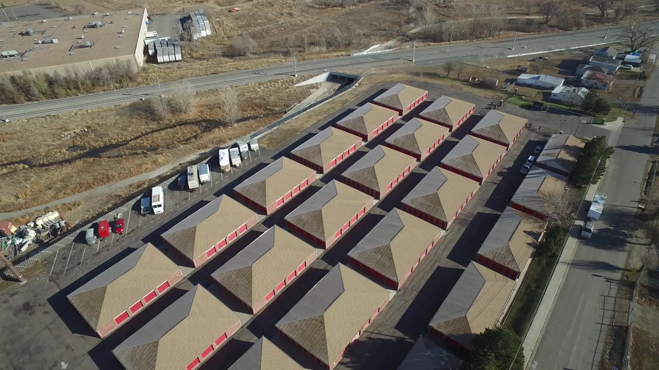 High aerial frame over Hidden Lake, Colorado, showing tan storage-building roofs, red roll-up doors, paved lanes, nearby roads, dry lots, parked vehicles, and no visible people.