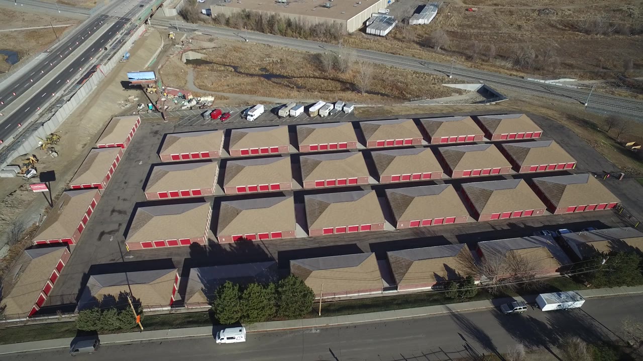 Aerial view in Hidden Lake, Colorado with the storage-like rows centered more tightly, red doors aligned along paved drives, roadside vehicles, bare ground, and no visible people.