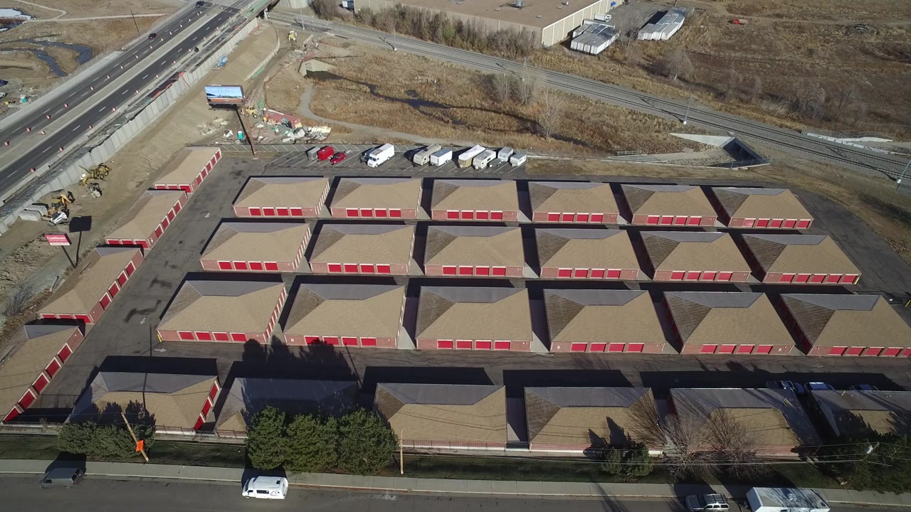 Aerial frame over Hidden Lake, Colorado with the storage rows centered, a diagonal road and ramp at the top, white trailers parked near the lot, and no visible people.