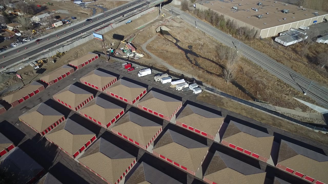 Aerial view in Hidden Lake, Colorado looking across a grid of tan roofs and red door rows toward roadside work vehicles, dry grass, and no visible people.