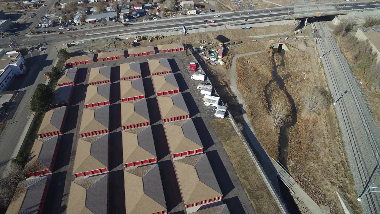 Overhead view of tan-roofed buildings beside a dry drainage channel and road corridor.