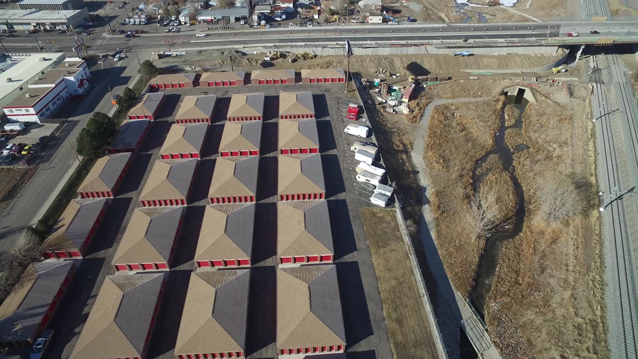 A slightly later overhead frame in Hidden Lake, Colorado shows the patterned tan roofs and red building fronts more centrally, with white vehicles parked along the right side and no visible people.