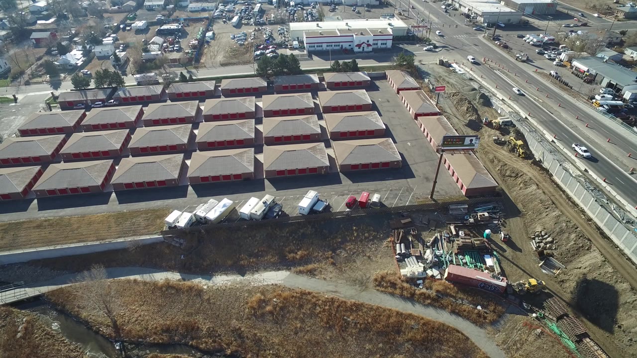 Drone view over Hidden Lake, Colorado, showing rows of red-doored commercial storage-style buildings, a roadside billboard, construction dirt, parked trailers, and no visible people.