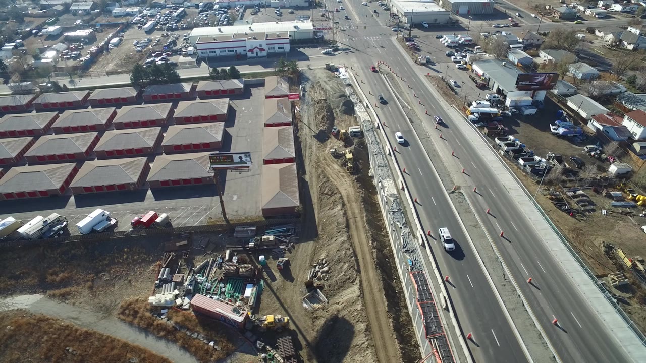 Aerial frame over Hidden Lake, Colorado showing a divided road with cars, orange cones, storage-style buildings, roadside construction, and no visible people.
