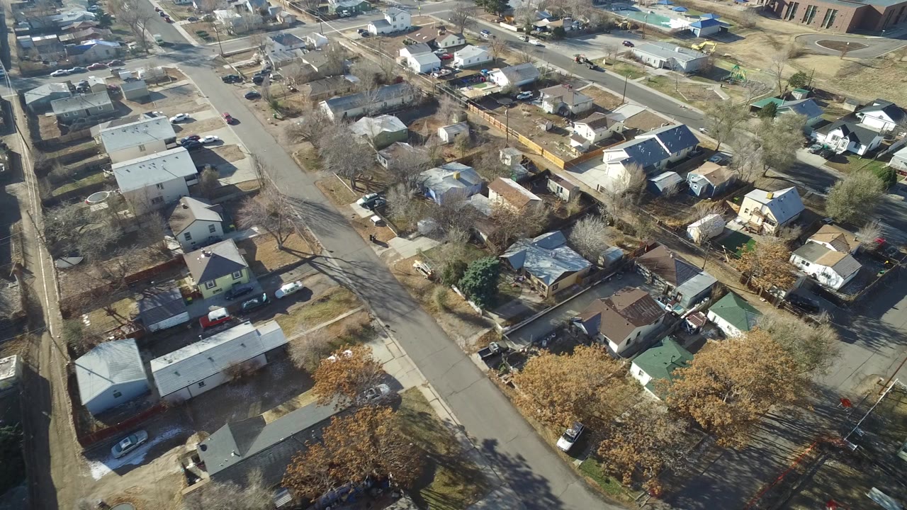 High oblique aerial view over Hidden Lake, Colorado homes, paved streets, fenced yards, parked cars, and leafless trees at the start of the clip.