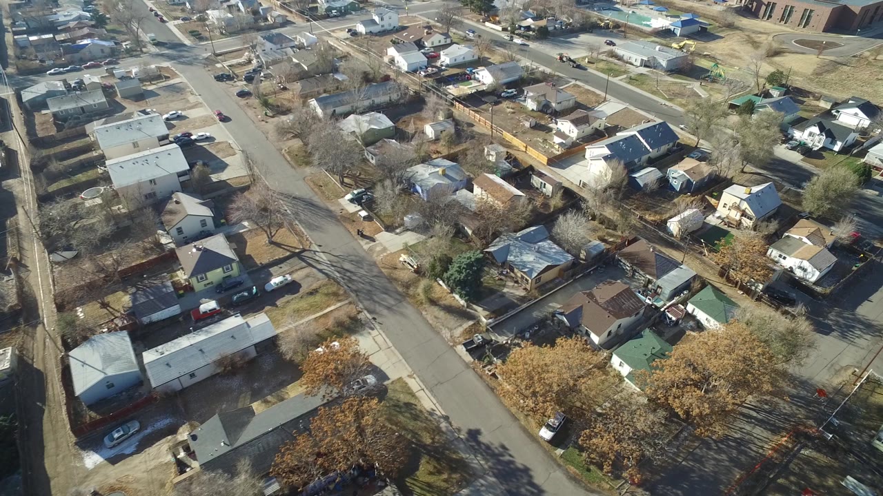 Aerial frame over Hidden Lake, Colorado with a diagonal street, compact houses, parked vehicles, winter lawns, and a larger building near the upper edge.
