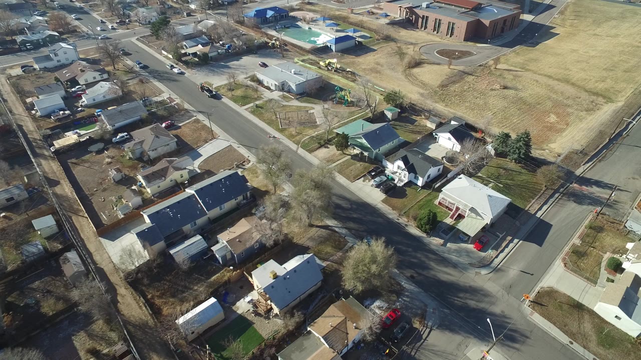 High aerial view over Hidden Lake, Colorado homes and intersecting streets, with a tan open field and larger brick building in the upper right, no visible people.