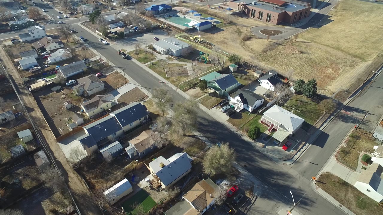 Aerial frame over Hidden Lake, Colorado showing clustered houses and yards in the foreground, a diagonal street through the center, and a broad tan field beyond it, no visible people.