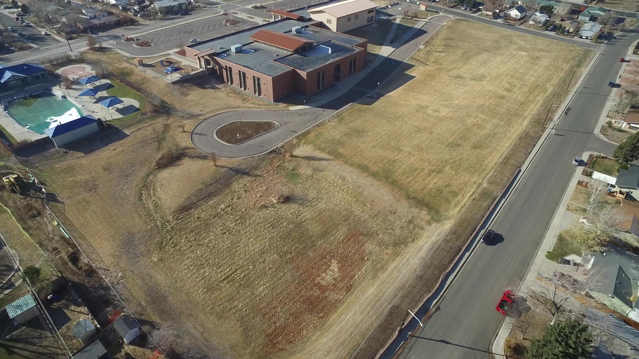 Drone view of a curved driveway, brick building, road, and dry field.
