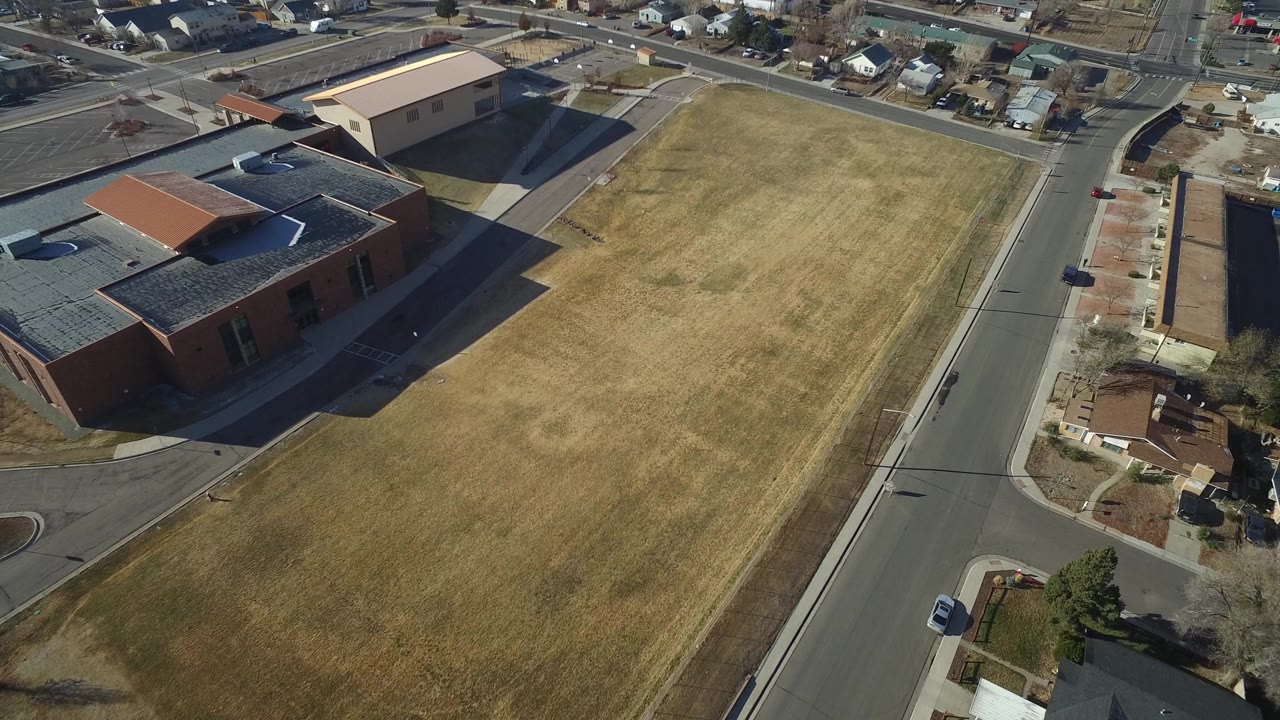 High aerial view of a dry grass field beside brick buildings and town roads.
