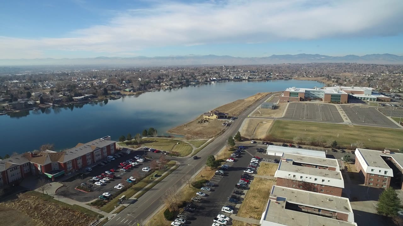 Aerial view of a lake, roads, parking lots, and low-rise buildings under bright sky.