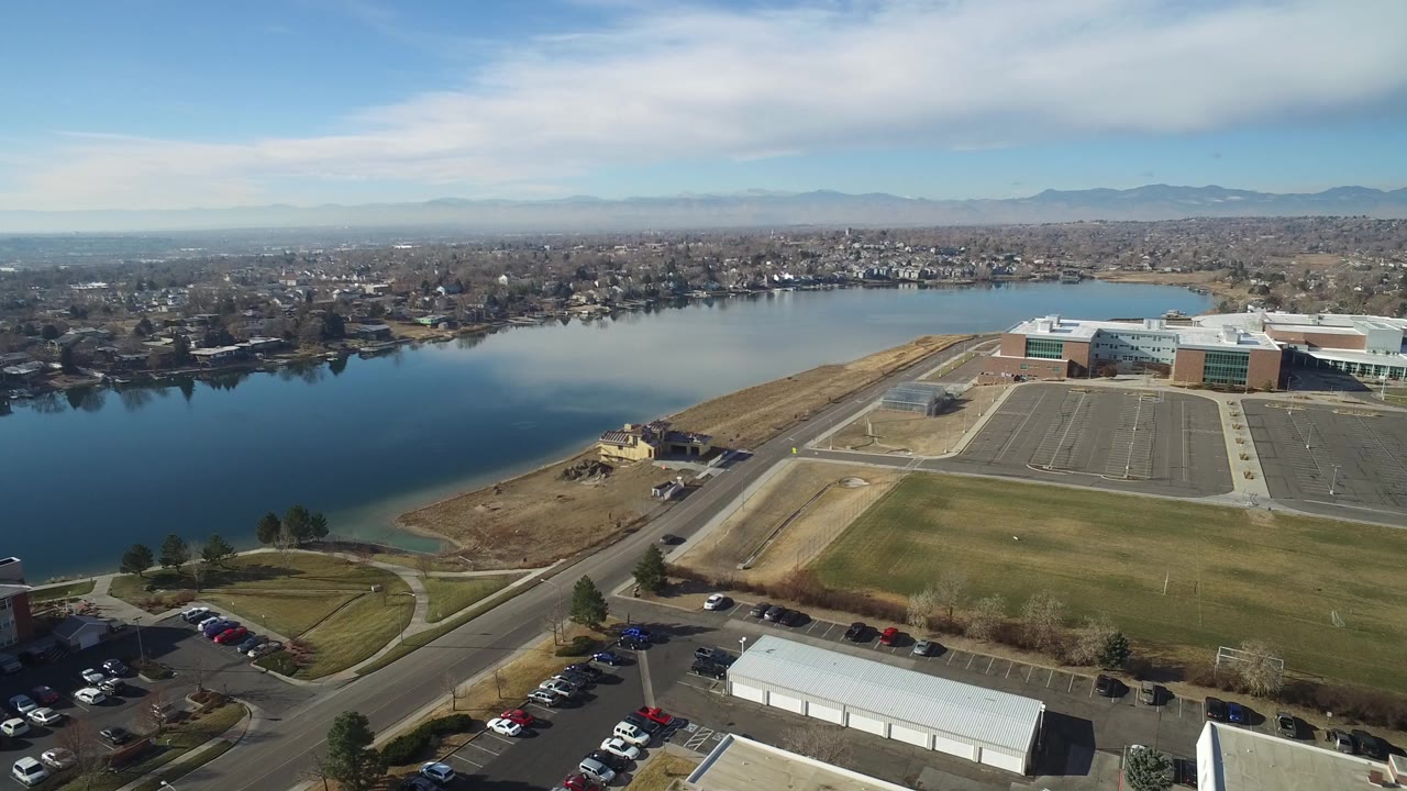 Aerial view of a lake beside roads, parking lots, grass fields, and a large building.