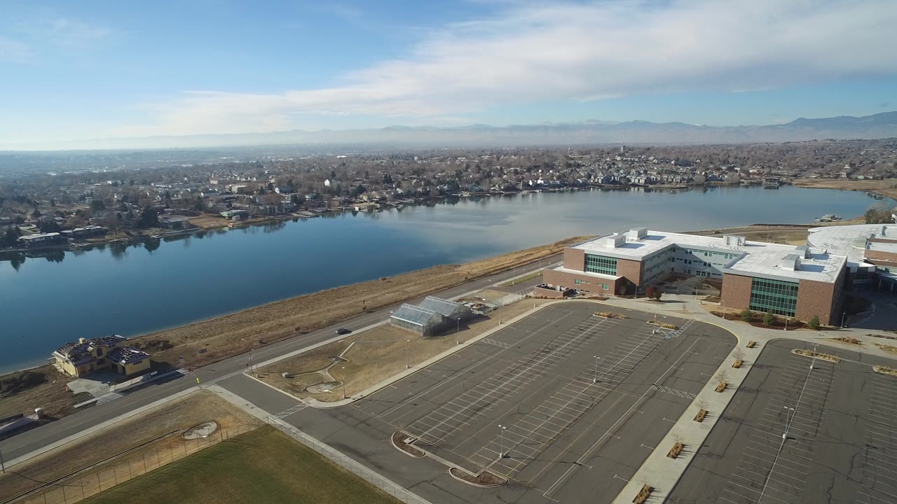 Aerial view of a lake, modern buildings, and an empty parking lot.