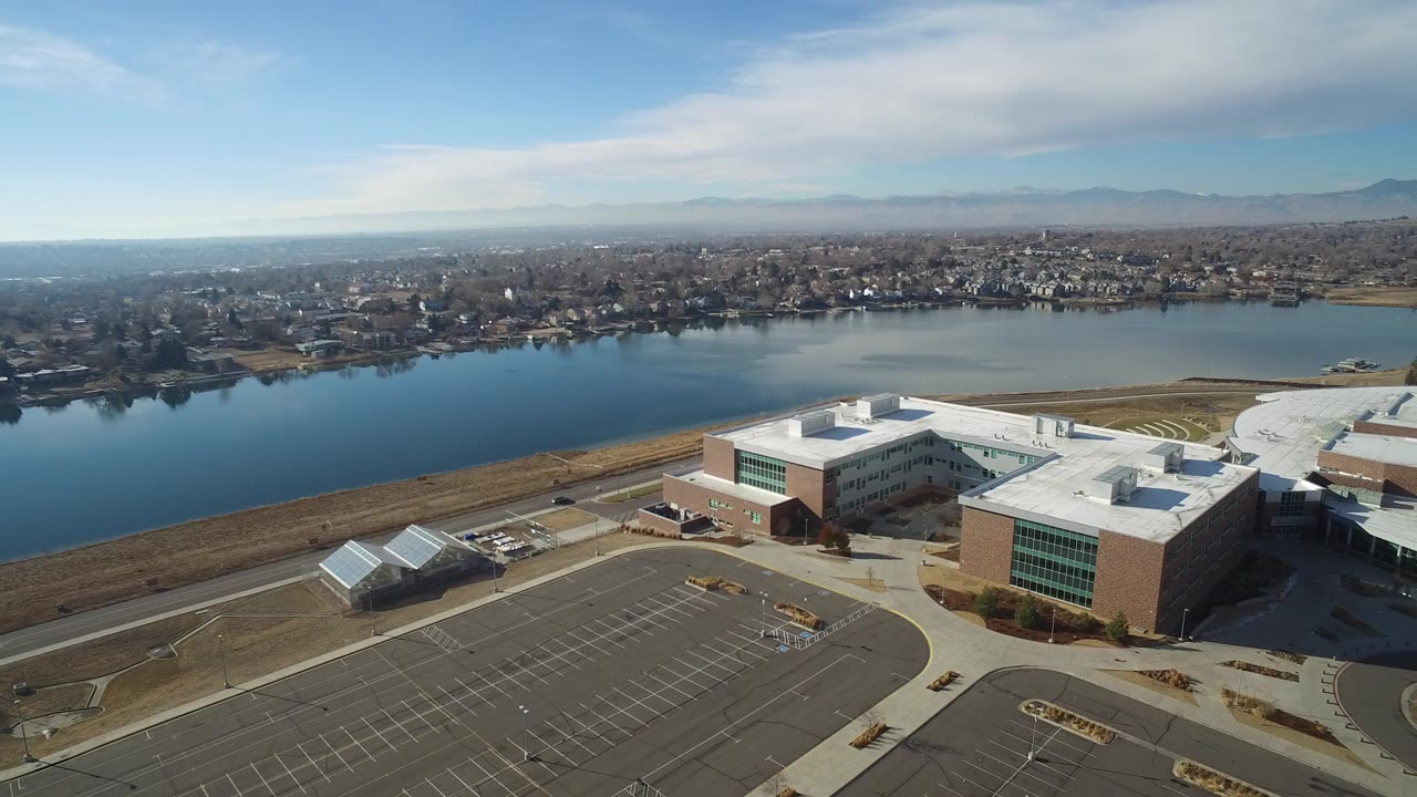 Aerial view of buildings, an empty parking lot, and a blue lake beyond.