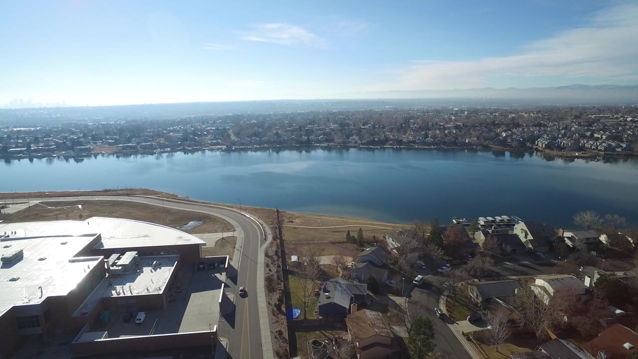 Aerial view of a lake beside rooftops and suburban homes.