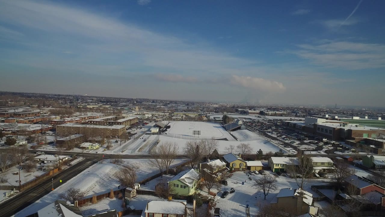Wide aerial view over Hidden Lake, Colorado with snowy houses in the foreground, low industrial buildings beyond, a distant horizon, blue sky, and no visible people.