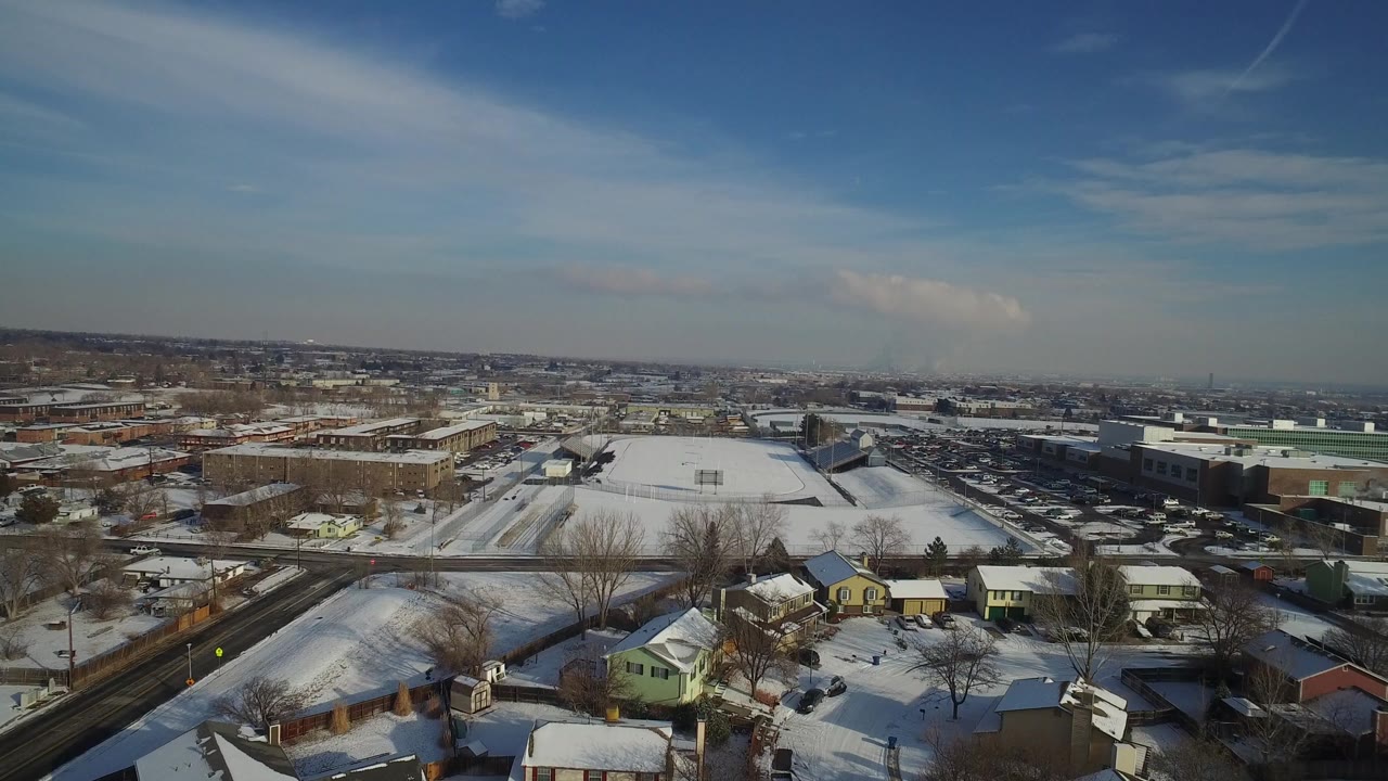 Hidden Lake, Colorado aerial frame showing snow on roofs and open lots, a road and rail corridor at left, low commercial buildings in the midground, and no visible people.