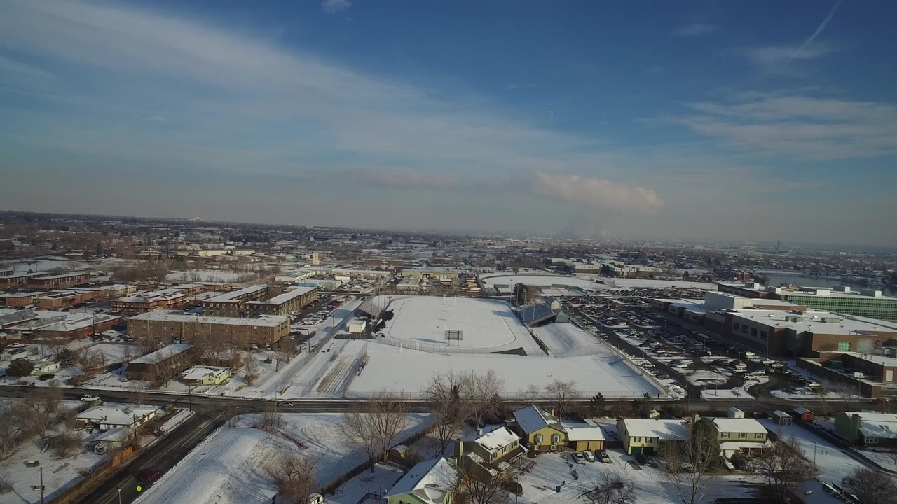 Aerial view of snow-covered neighborhood streets and low buildings under blue sky.