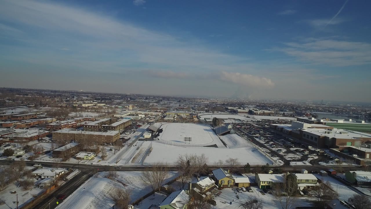 Aerial frame over Hidden Lake, Colorado showing snow on rooftops and roads, a broad parking area near low buildings, bare winter trees, and no visible people.