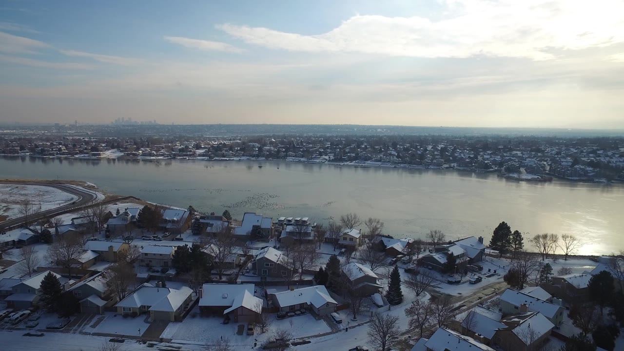 Snowy homes and trees line a lake with a distant skyline on the horizon.