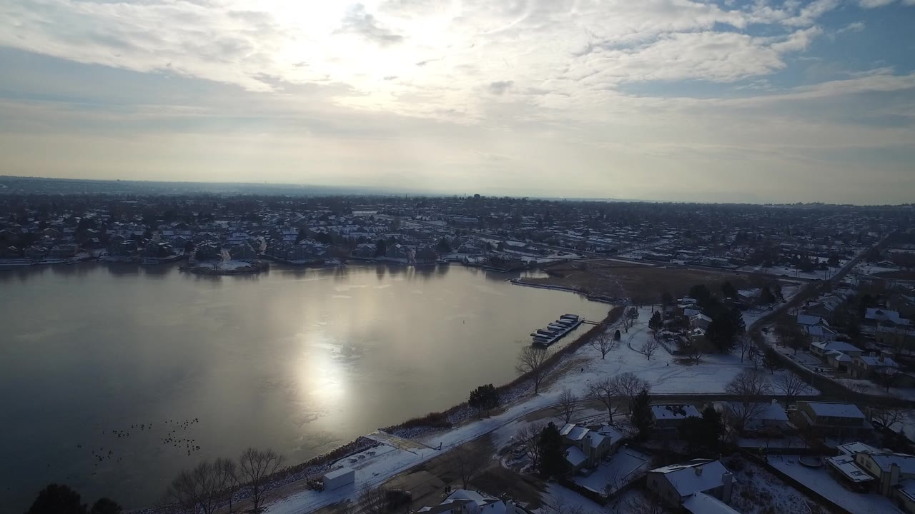 Aerial view of a snowy lakeshore with homes and roads under a bright winter sky.