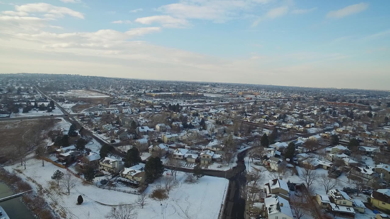 High aerial view over Hidden Lake, Colorado, showing snow-dusted homes, curving streets, leafless trees, a dark water edge, and no visible people.