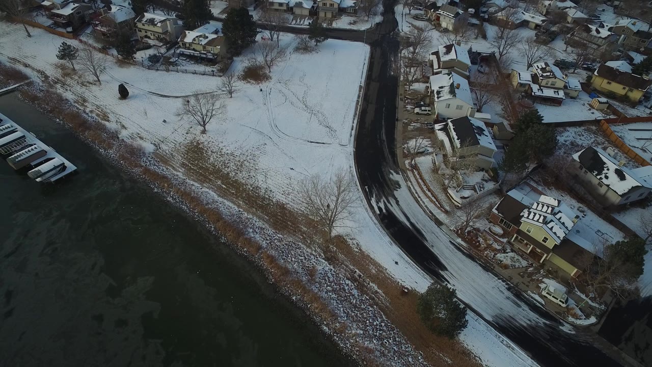 Aerial view of a snowy lakeside neighborhood and curved road.