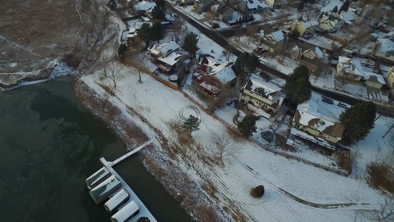 High aerial view in Hidden Lake, Colorado showing snow-covered private homes, a shoreline, dark water, a dock, bare trees, and no visible people.