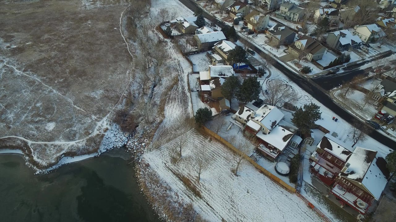 Aerial view of snowy homes beside a lake and open field