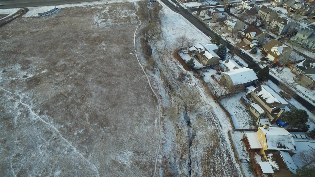 High overhead view of an icy field in Hidden Lake, Colorado, with snowy residential roofs along the edge, a road at the top of frame, and no visible people.