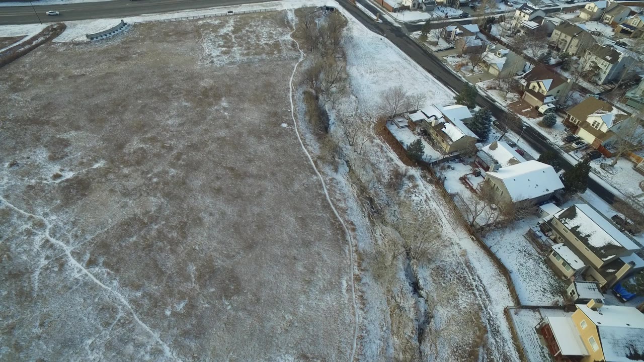 Top-down winter field with nearby homes and cars on a distant road.