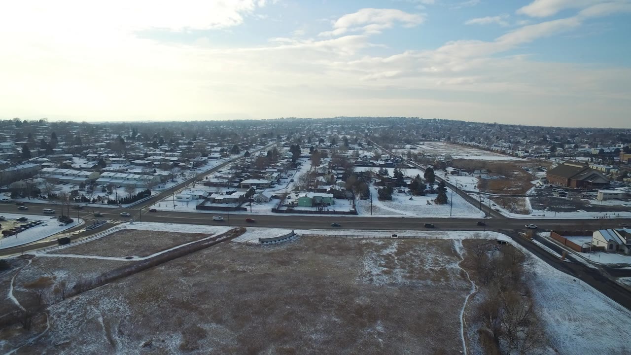 Opening aerial frame over Hidden Lake, Colorado showing a snow-dusted open field, curving road, residential blocks, bare trees, and no visible people.