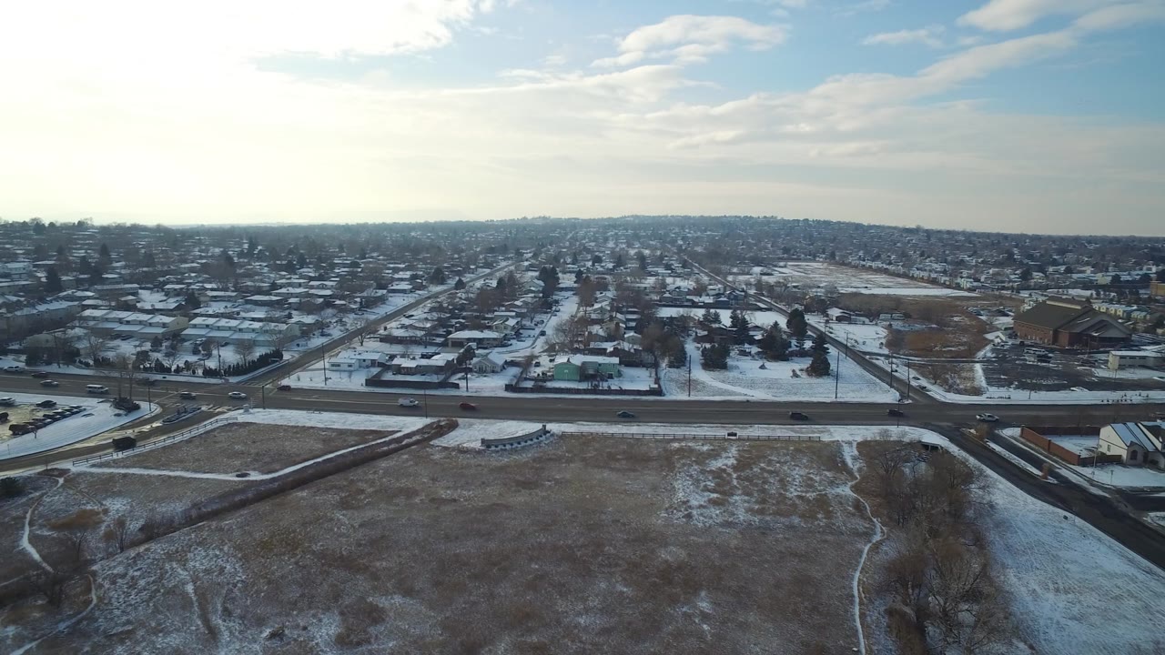 Aerial frame in Hidden Lake, Colorado with open snowy ground in the foreground, a road crossing the middle, clustered homes beyond it, and no visible people.