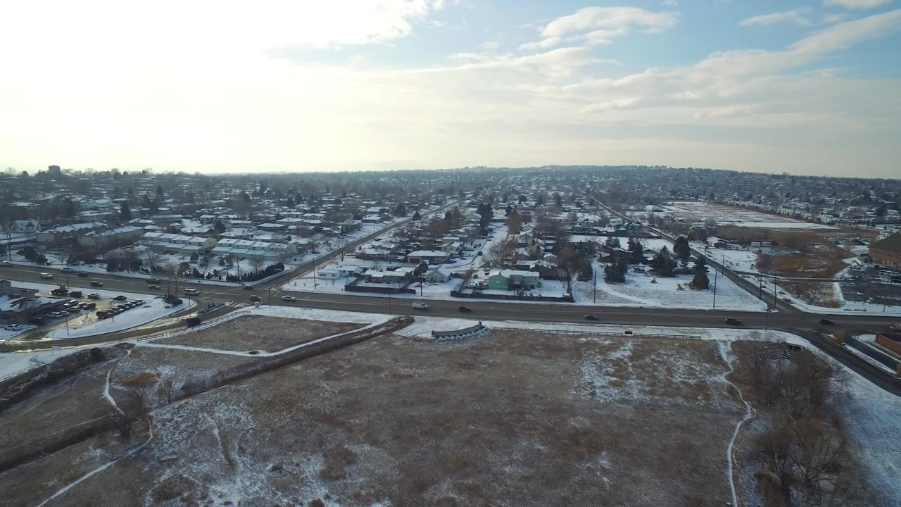 Drone-height view across a snowy neighborhood with open land and bright sky.