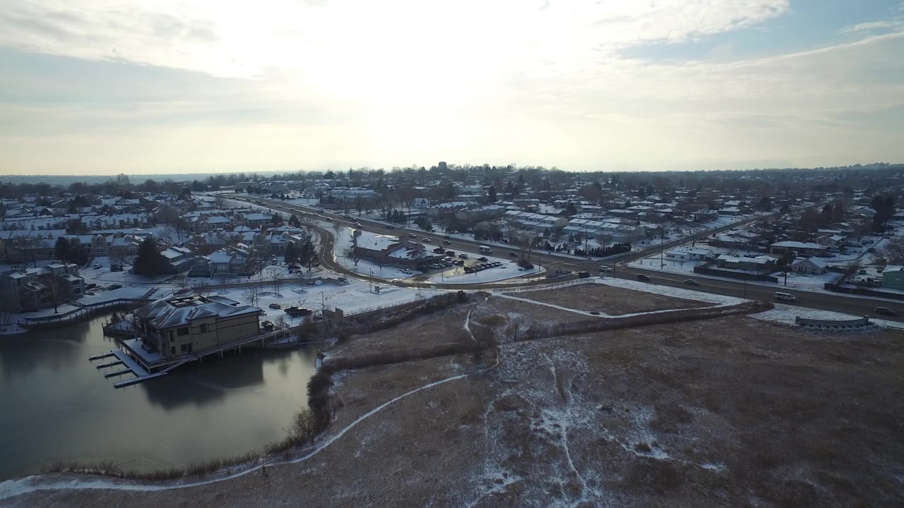 Aerial view in Hidden Lake, Colorado looking across calm winter water toward snow-covered streets, clustered homes, docks, and no visible people.