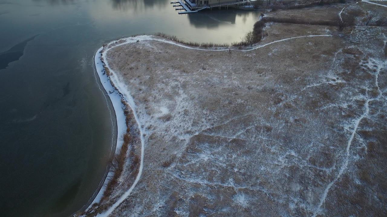 Snow-dusted shoreline curves around dark lake water from above.