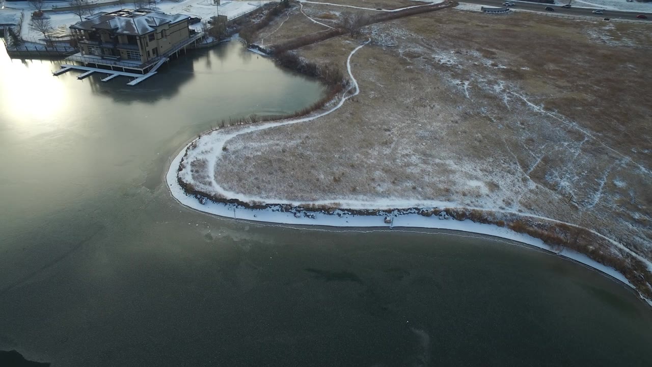 Aerial view of a snowy curved shoreline beside green-gray lake water.
