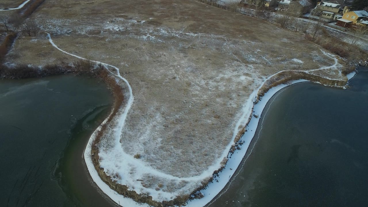 Aerial view of a snow-edged lake peninsula and brown winter grass.