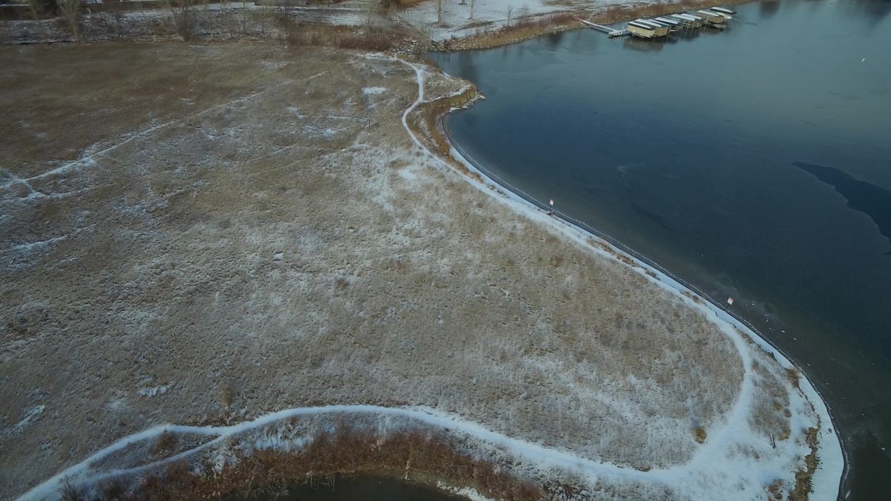 Drone-style overhead view of lake water and snow-dusted shore