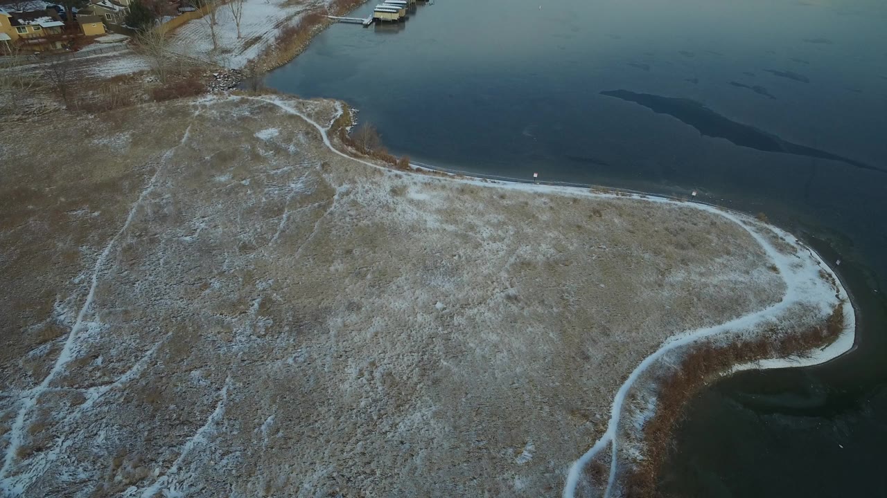 Aerial view of a snow-dusted shoreline curving around dark lake water.