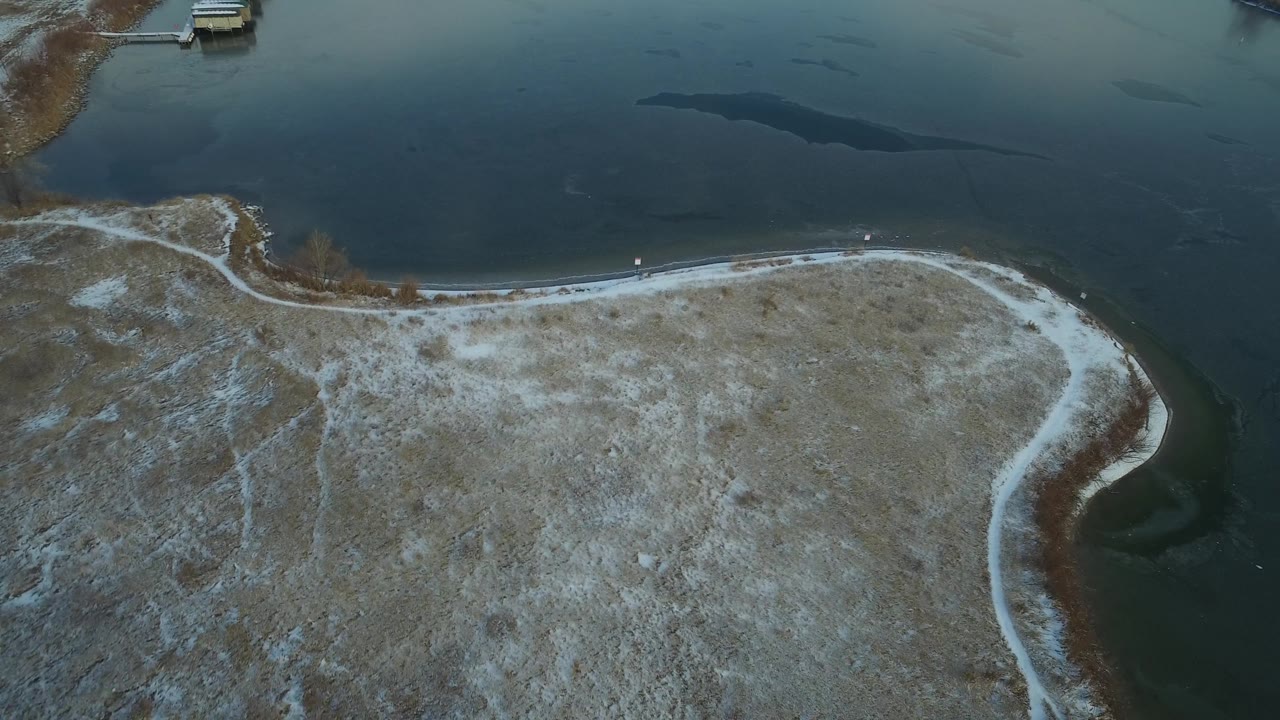 Curved winter shoreline with dark patches in lake water.