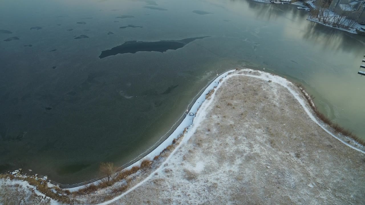 Overhead Hidden Lake frame with the curved snowy land edge centered below open blue-green water and residential docks visible near the upper edge.