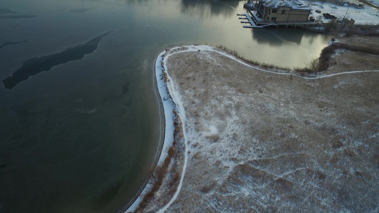 Drone view of lake water surrounding a curved snowy peninsula.