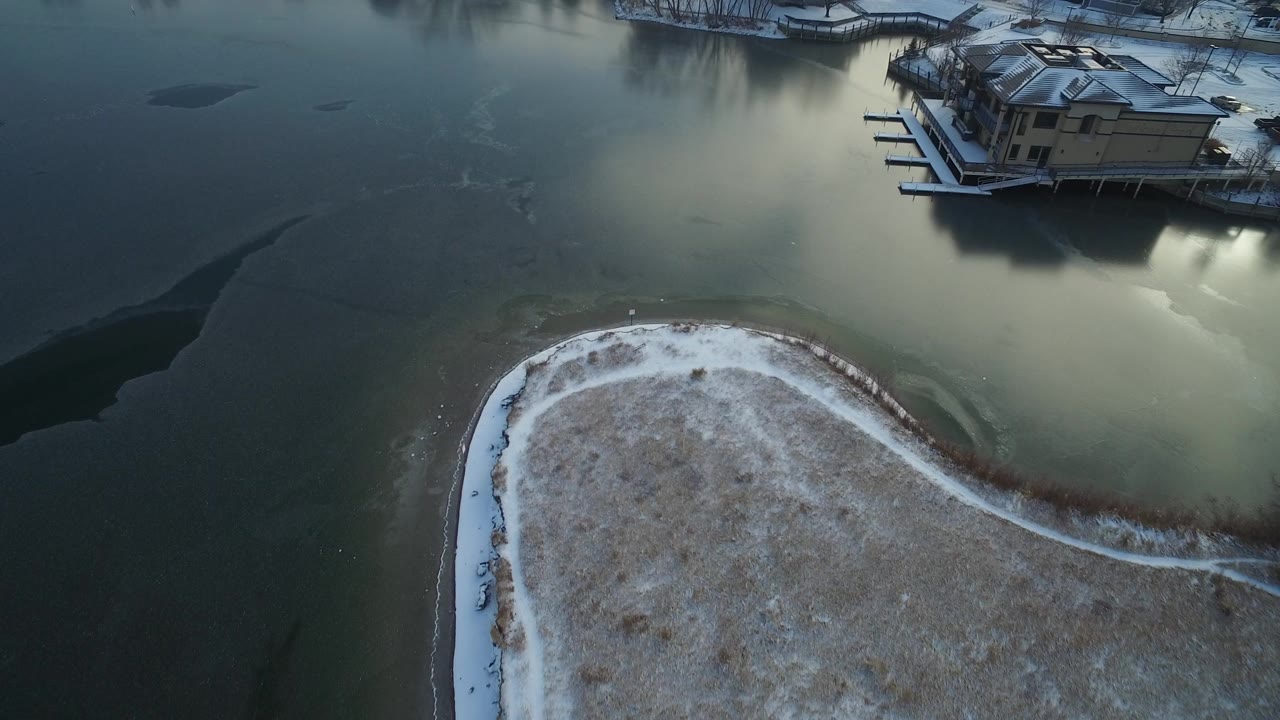 Aerial view of frozen water beside a snowy shoreline and waterfront homes.