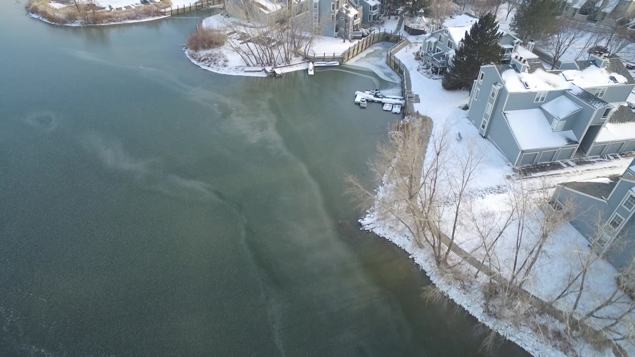 Overhead lake cove with snow, homes, docks, and leafless shoreline trees