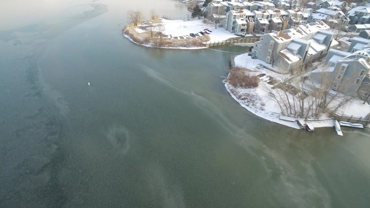 Aerial view of snowy lakeside homes beside green-blue water.