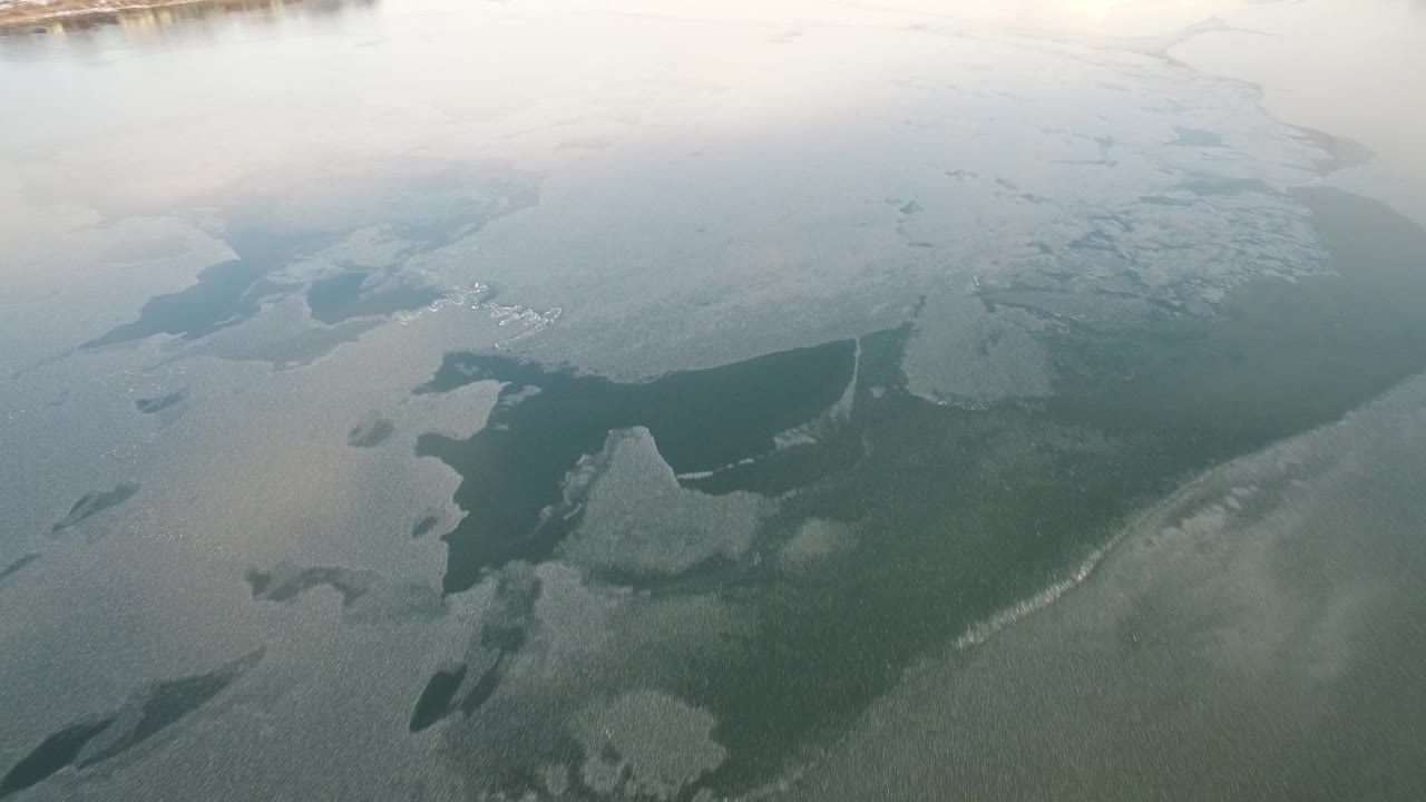 Aerial frame over Hidden Lake, Colorado, showing pale ice sheets and dark open-water gaps with no visible people.