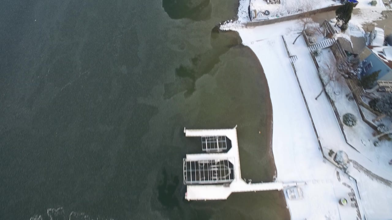 High overhead view in Hidden Lake, Colorado showing green-gray lake water, snow-covered shoreline, docks, and portions of residential yards with no visible people.