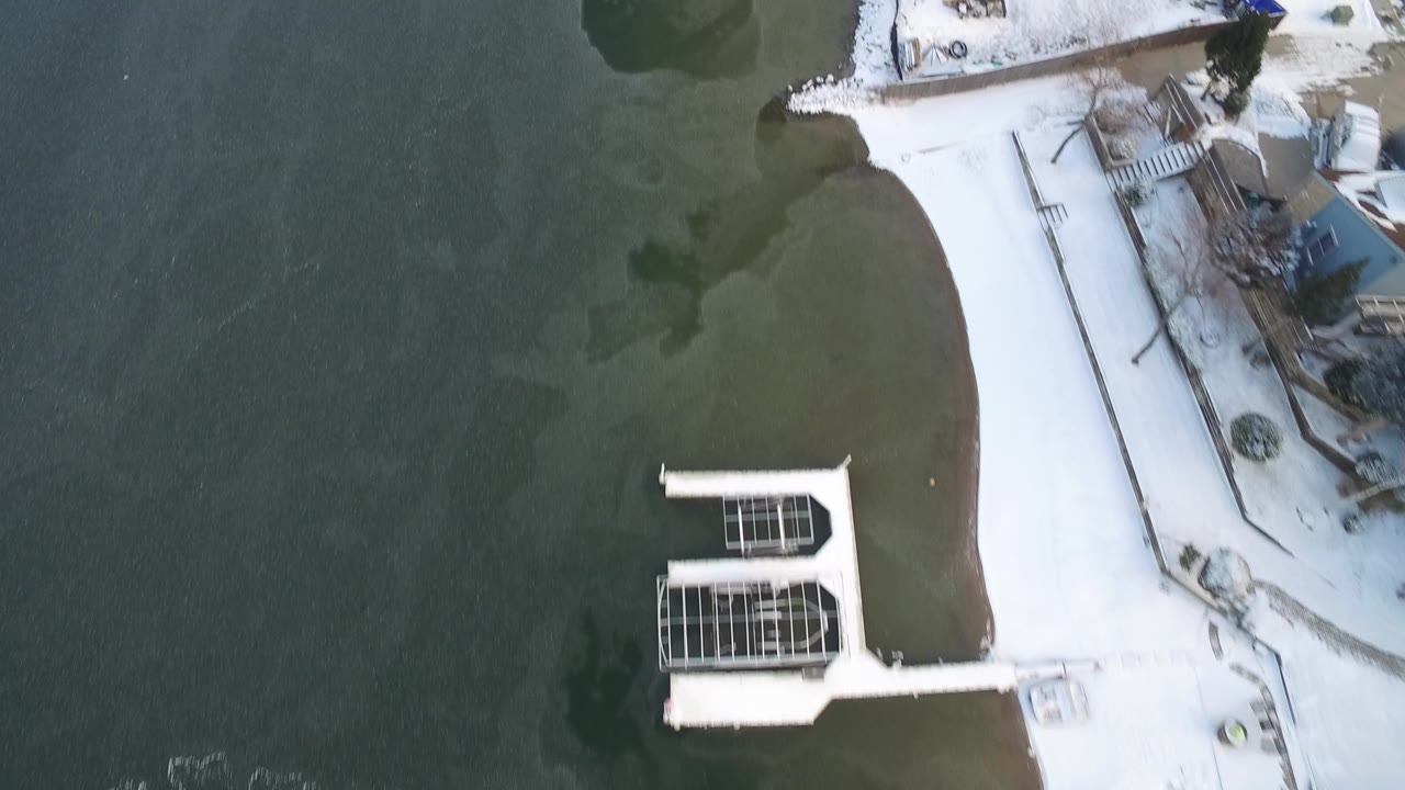Aerial frame in Hidden Lake, Colorado with two rectangular docks near snow-covered yards and green lake water, with no visible people.