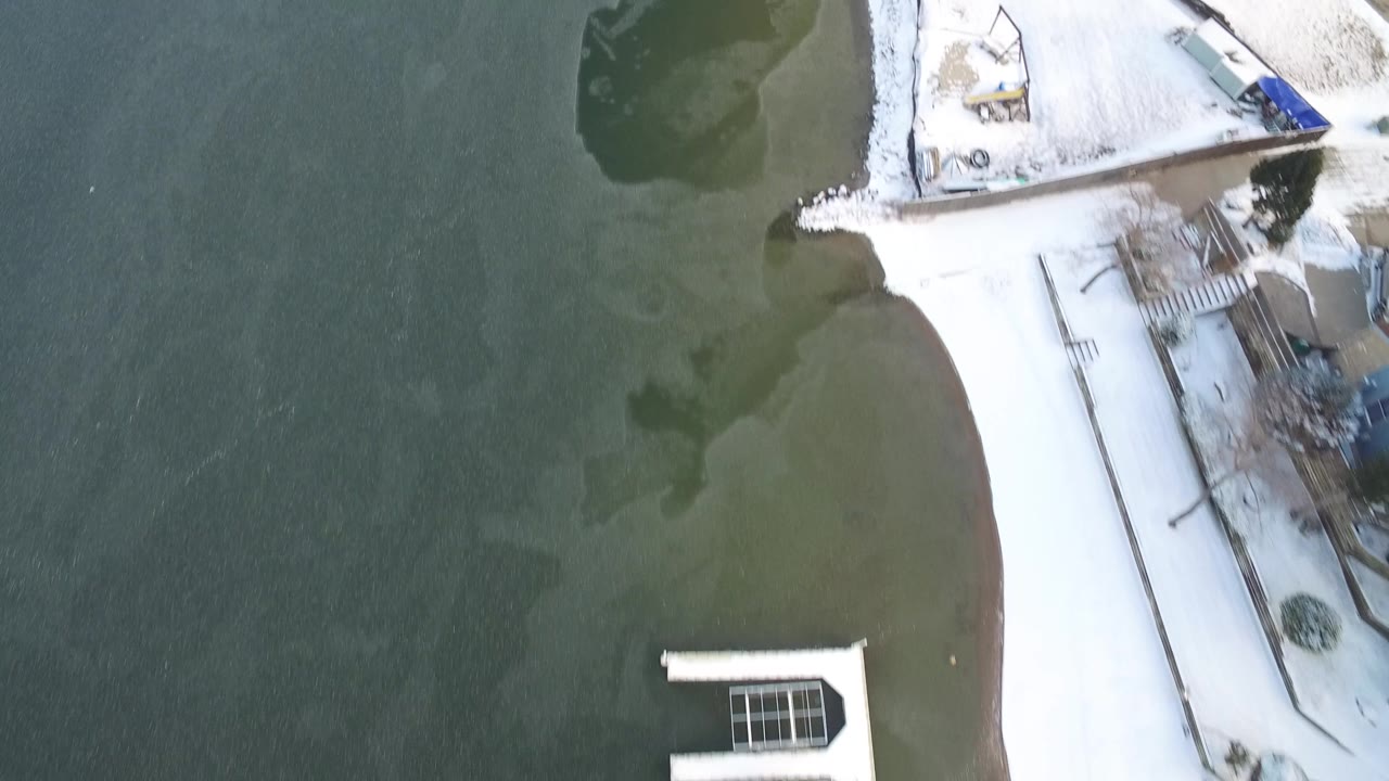 Top-down winter shoreline with a snowy yard, dock, and lake shallows.